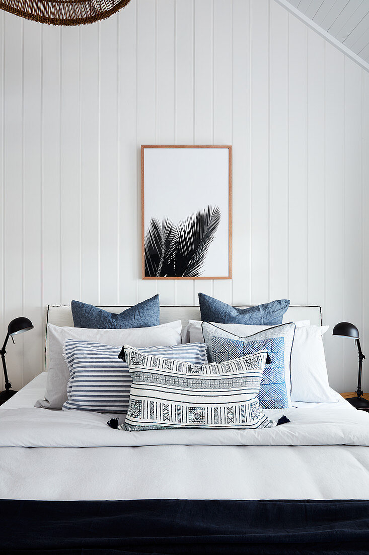Doppelbett mit blauer Tagesdecke im Schlafzimmer mit weißer Holzverkleidung