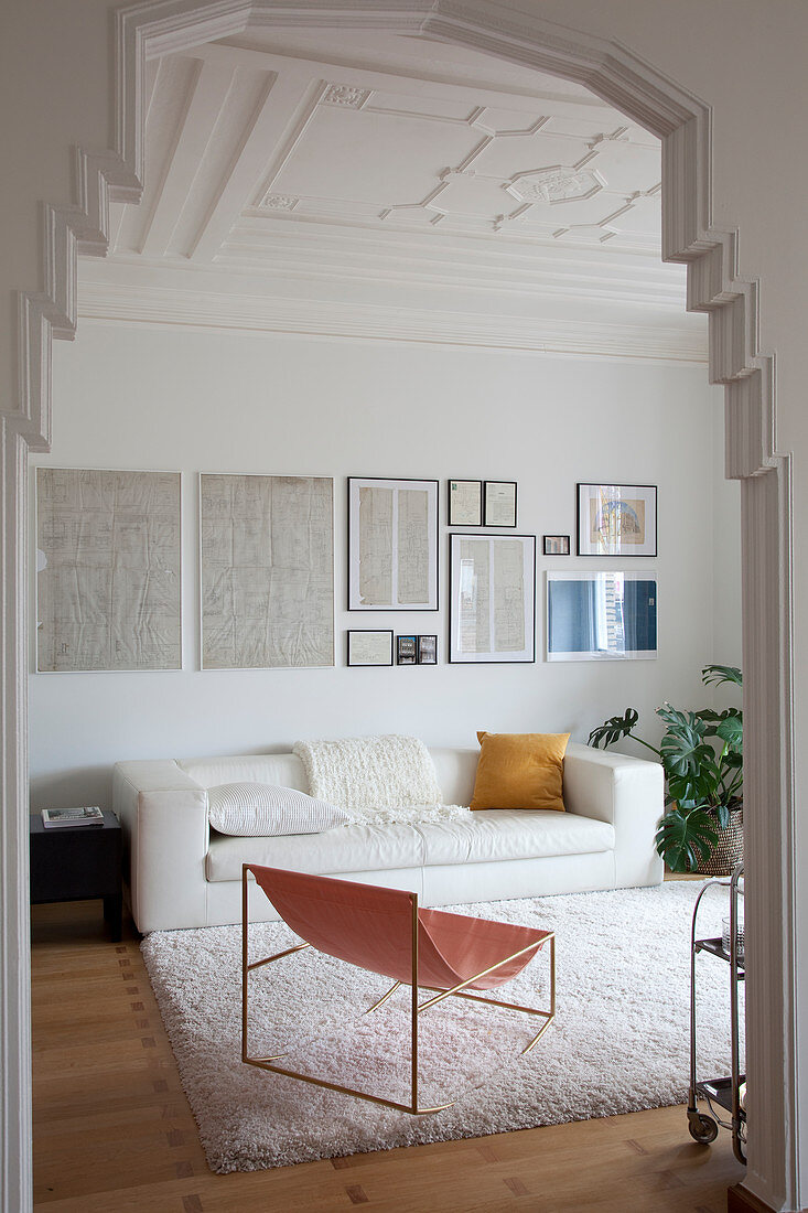 Blick ins Wohnzimmer mit weißer Ledercouch, darüber alte Skizzen an der Wand