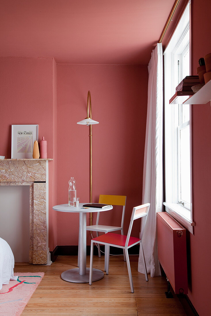 Small seating area next to disused fireplace in bedroom with salmon-pink walls