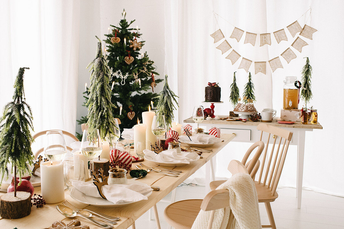 Weihnachtlich gedeckter Tisch mit weißen Stumpenkerzen und kleinen Tannenbäumchen