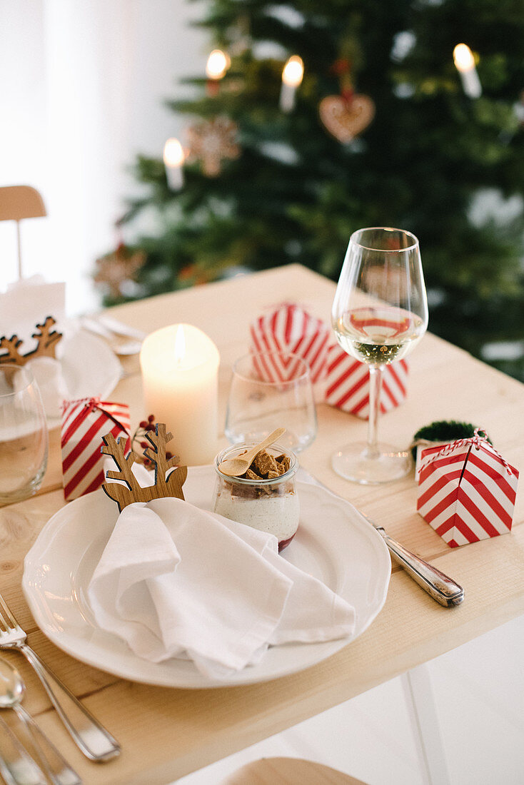 Christmas place setting with gingerbread mousse in glass bowl and favours in red-and-white striped boxes