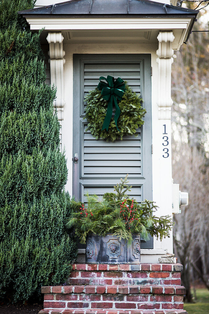 Front door decorated with Christmas wreath and Christmas arrangement on steps