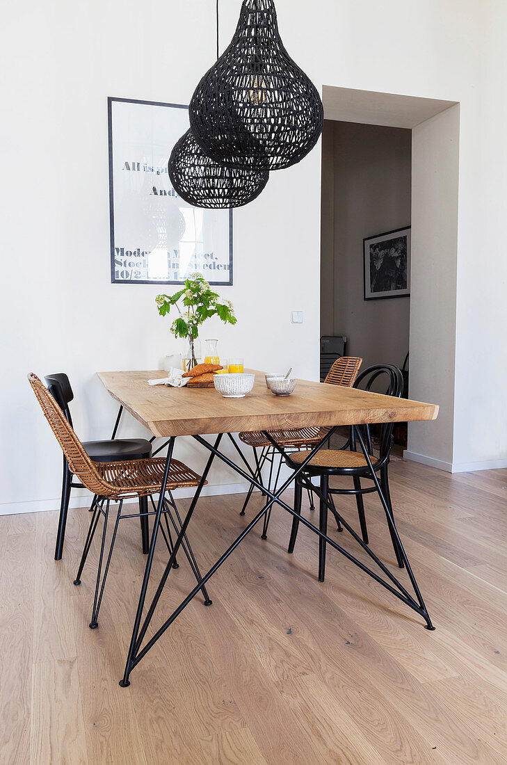 Dining table and various chairs below black pendant lamps