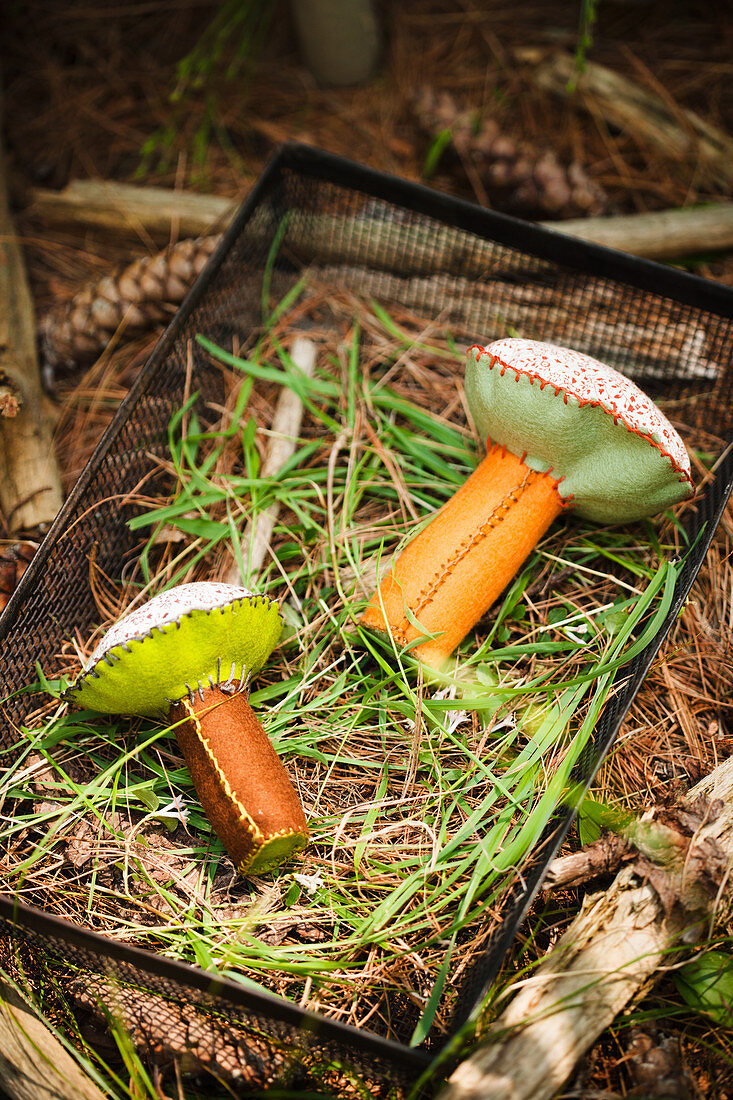 Hand-sewn felt and fabric mushrooms on grass in metal basket