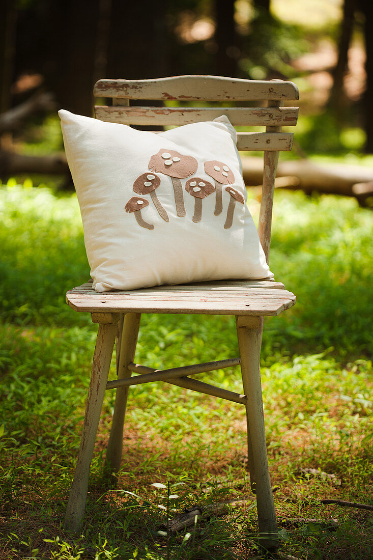 Kissen mit Pilzdekor auf einem Stuhl in einer sonnigen Waldlichtung
