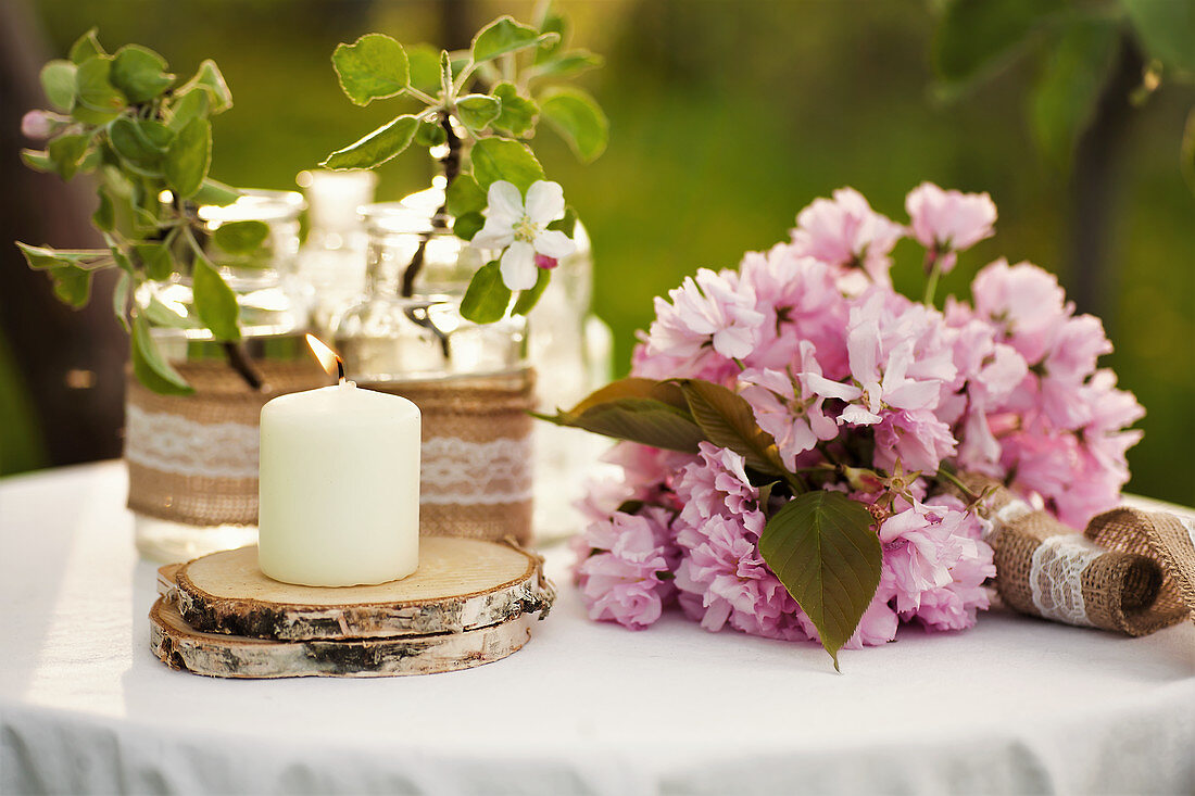 Candle on wooden coaster, cherry blossom and peonies on garden table
