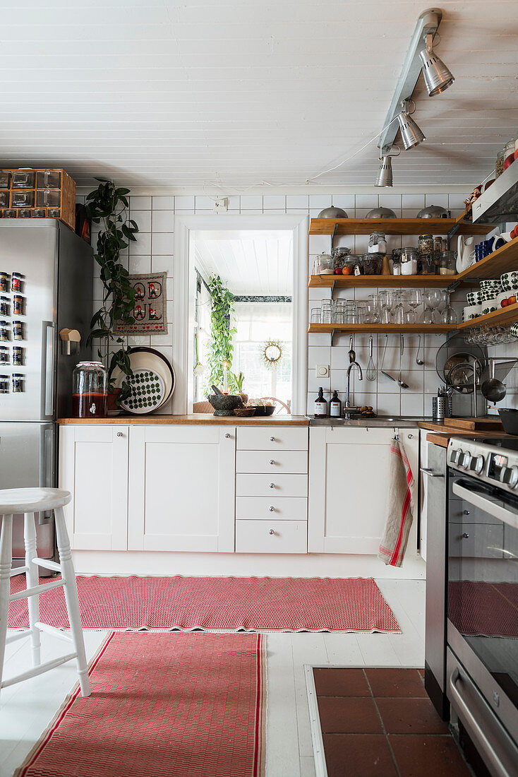 Shelves on walls above base units in bright kitchen with pink rugs