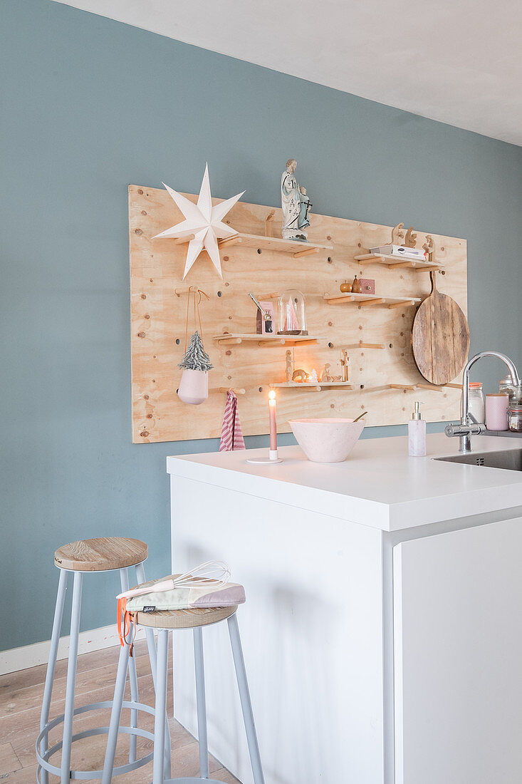 White island counter, bar stools and ornaments on DIY wooden shelves on pale blue wall