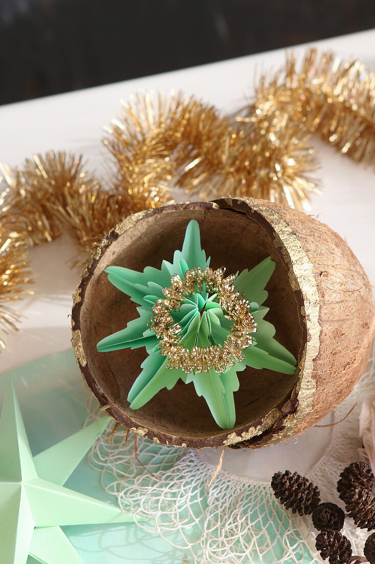Gefalteter Stern aus grünem Papier in vergoldeten Kokosnussschalen