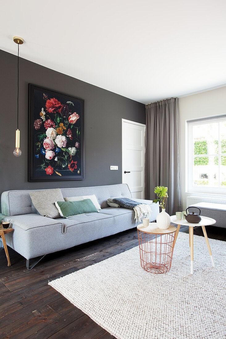 Grey sofa with scatter cushions below floral painting in living room