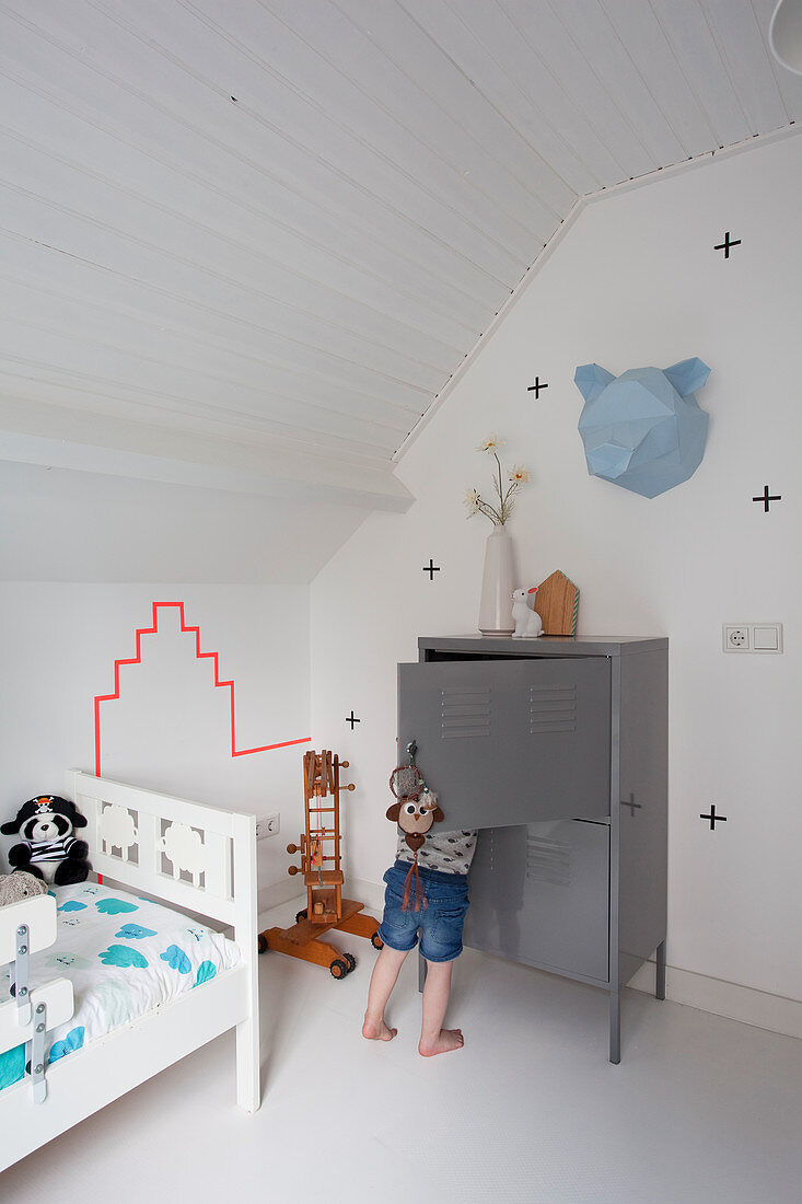 Kind vor grauem Schrank und weißes Bett im Kinderzimmer im Dachgeschoss