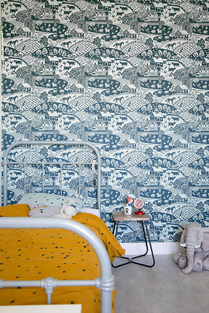 Grey metal bed against blue-patterned retro wallpaper