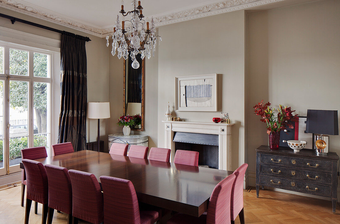 Pink upholstered chairs at long table in classic dining room with fireplace