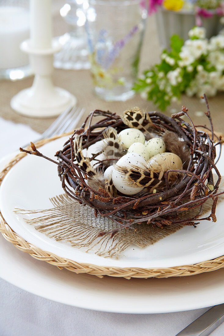 Osternest mit gesprenkelten Eiern und Federn als Tischdeko