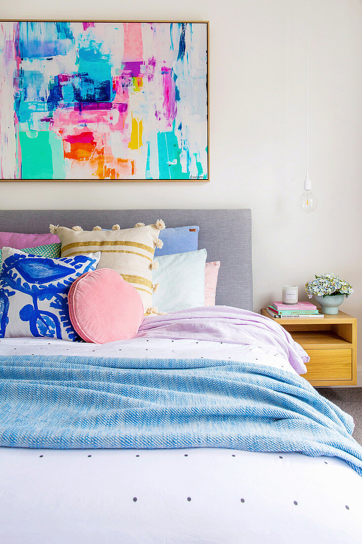 Colorful painting over the bed with lots of different pillows