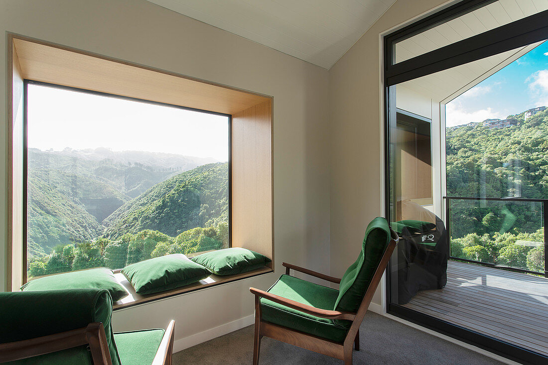 Grüne Polstersessel und passende Kissen auf Fensterbank vor Panoramafenster mit Landschaftsblick