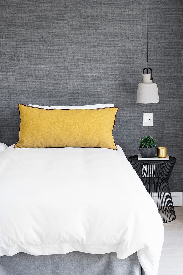 Yellow pillow on bed against grey wall