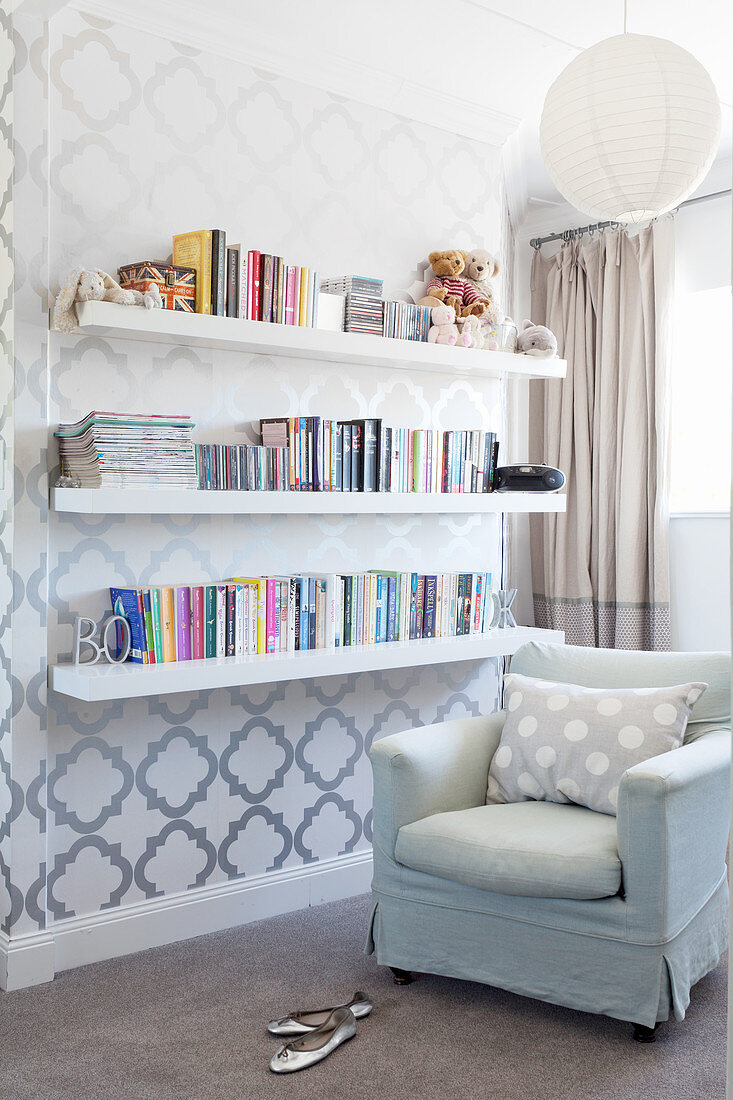 Armchair, books on shelves mounted on wall with patterned wallpaper in corner of room