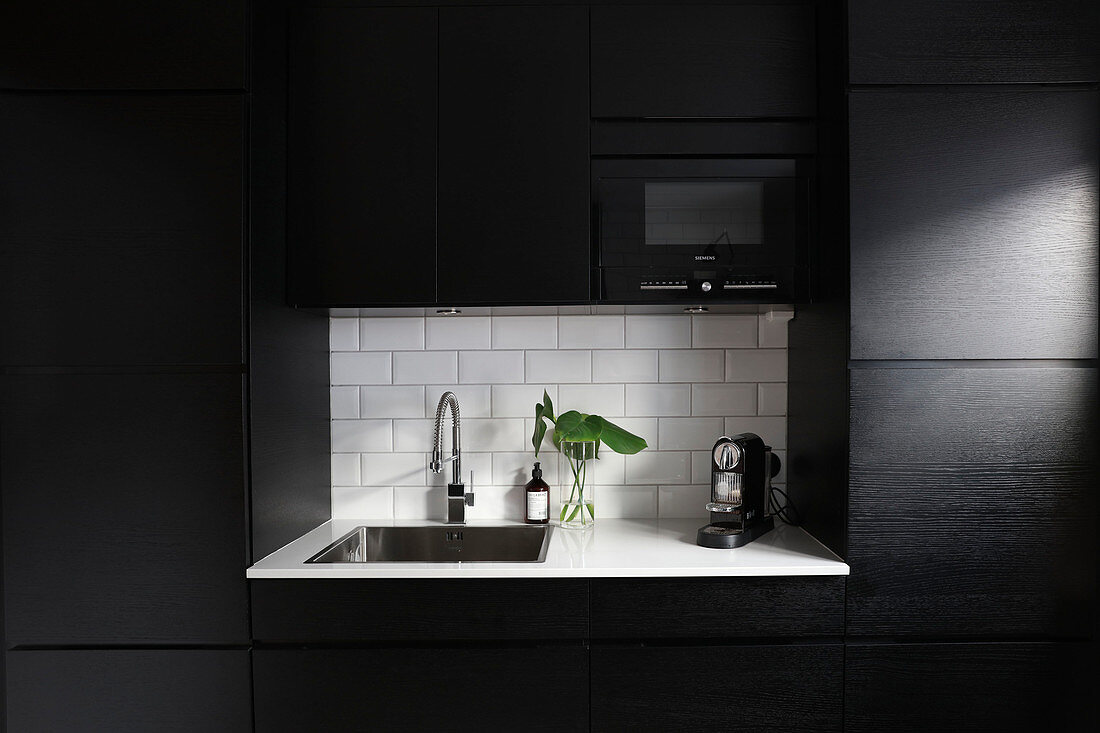 Modern, black fitted kitchen with white worksurface in niche