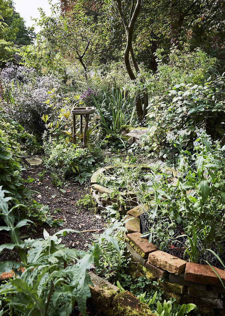 Round bed edged with brick in mature, natural-style garden