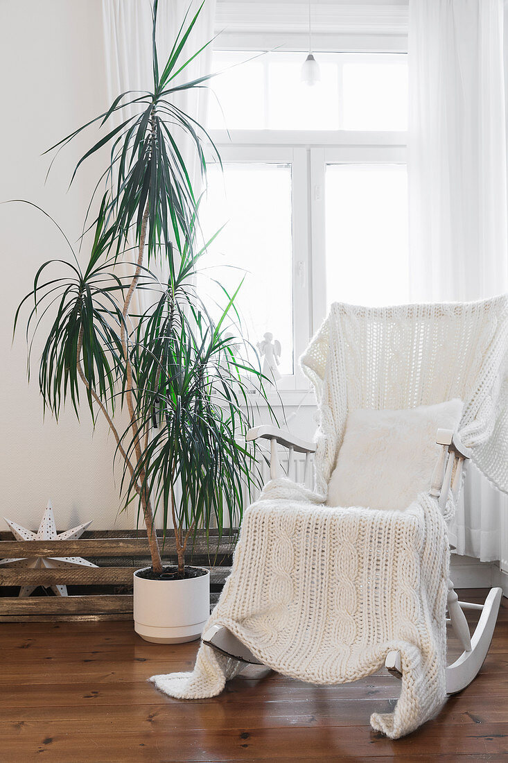 White knitted blanket on rocking chair next to potted palm