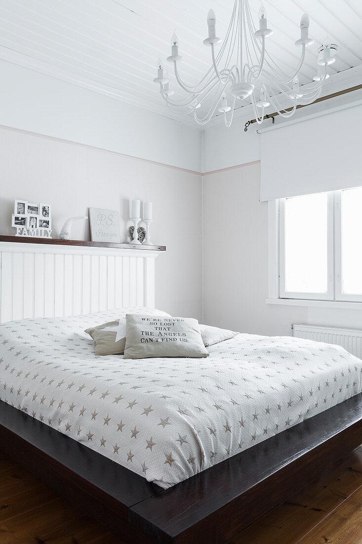 Doppelbett mit Kopfteil aus Holz und weißer Kronleuchter im Schlafzimmer