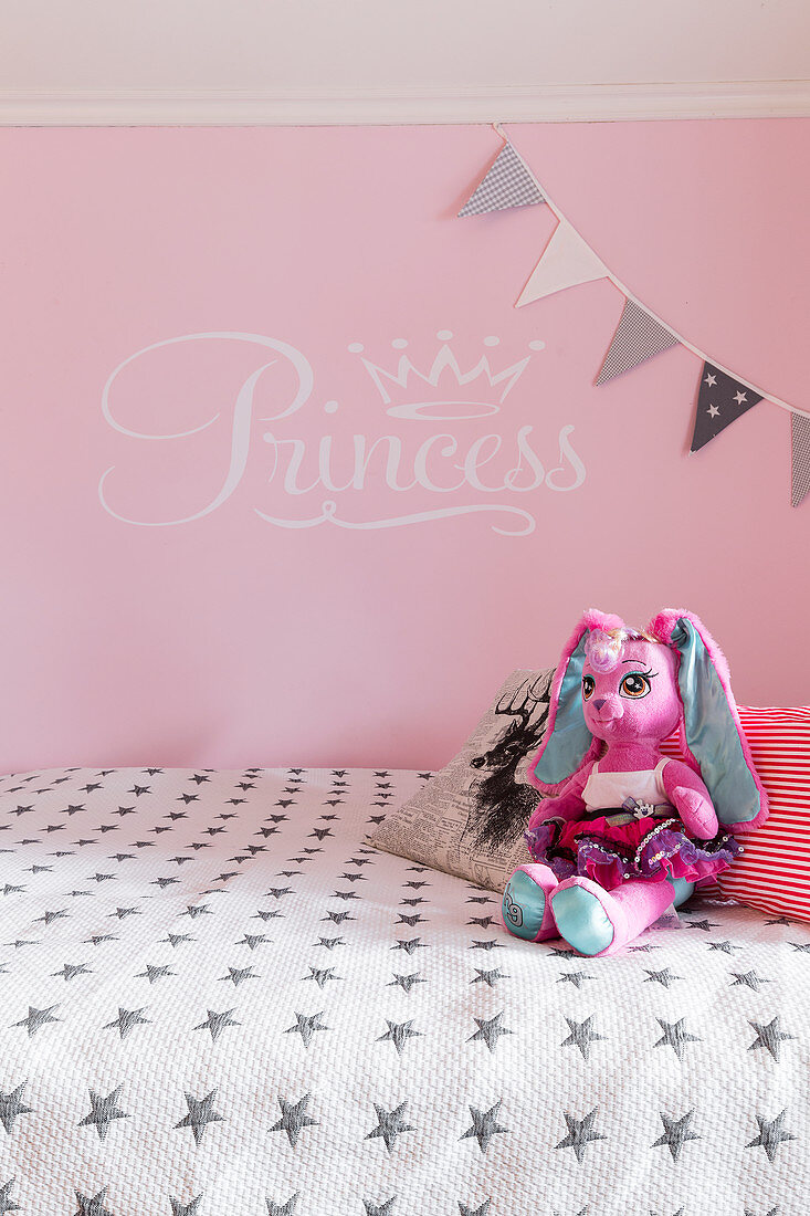 Plüschfigur auf Bett vor rosa Wand im Mädchenzimmer