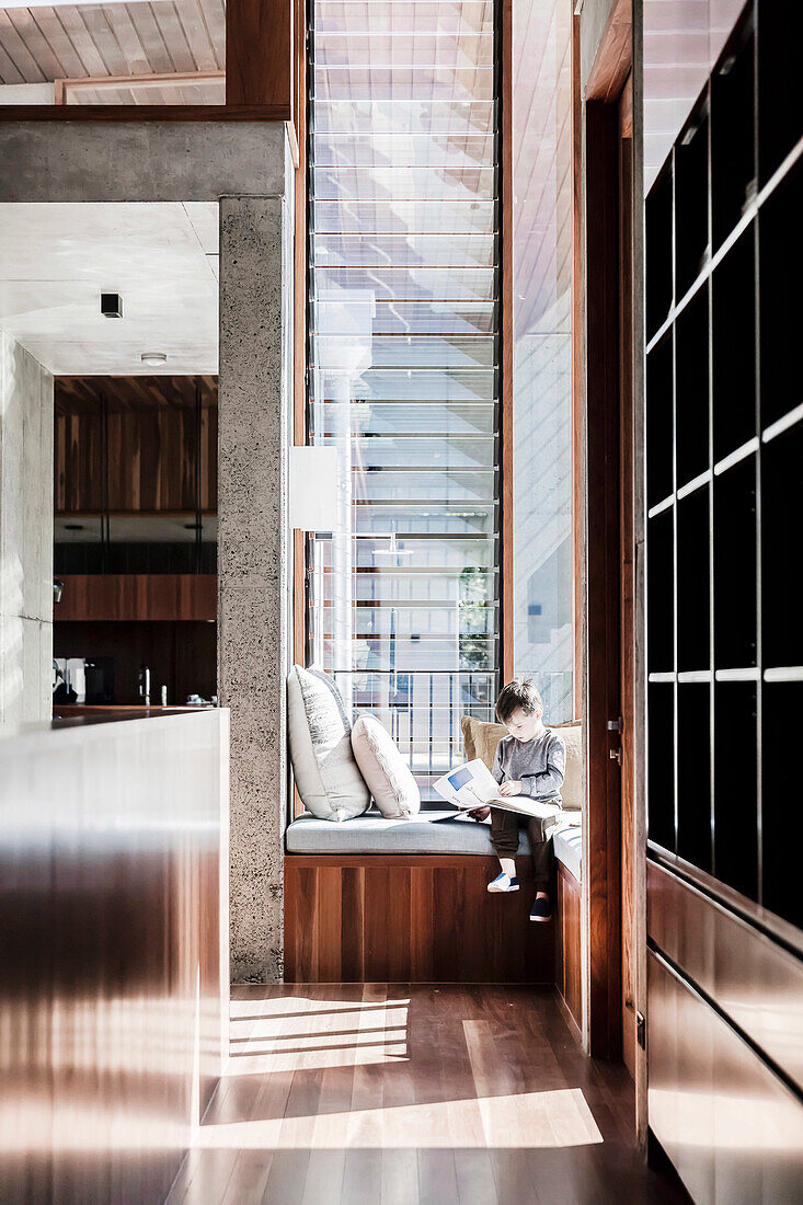 Boy sits on custom bench in front of window in high room