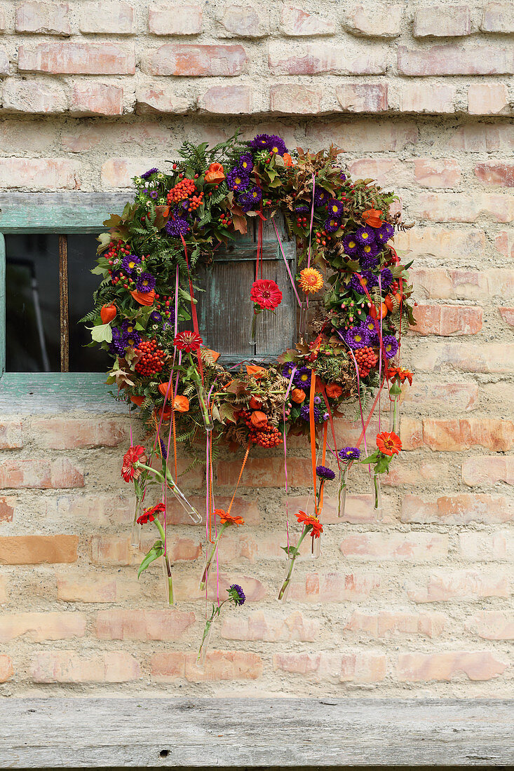 Autumnal wreath of flowers with test tubes hung from ribbons on brick wall