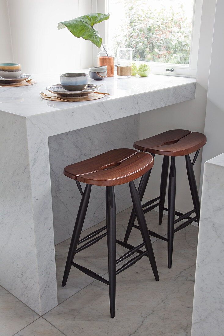Two stools below crockery in earthy shades on marble table