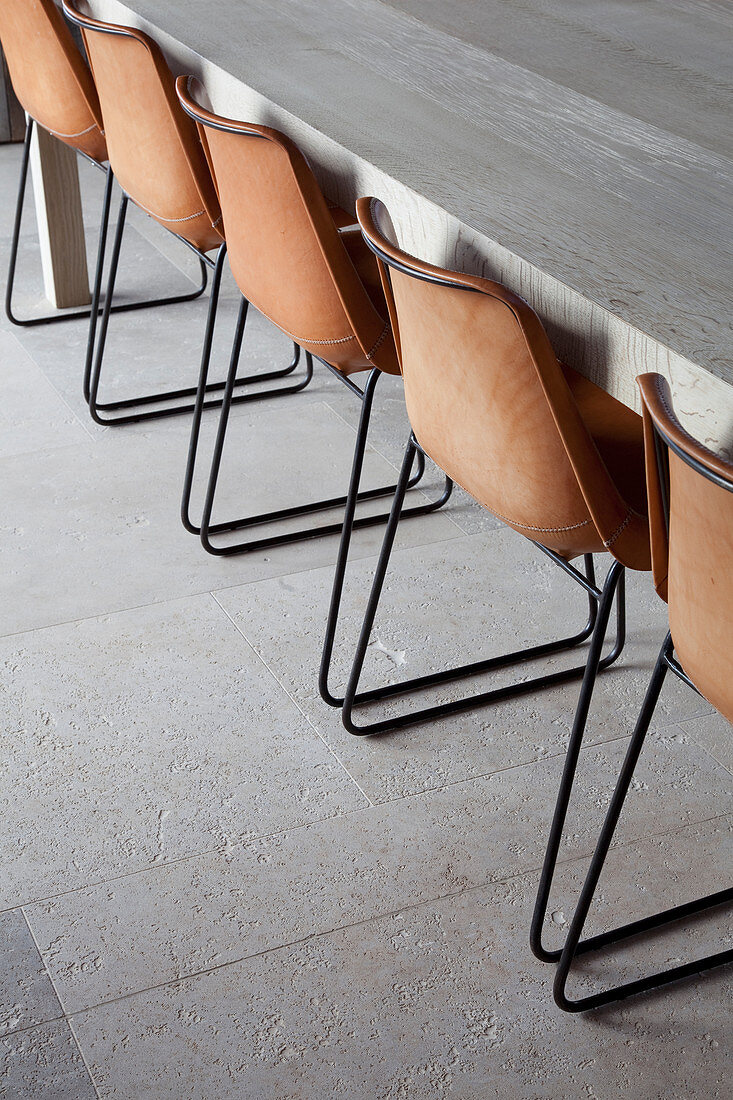 Braune Stühle mit Metallgestell am langen Esstisch auf Natursteinboden