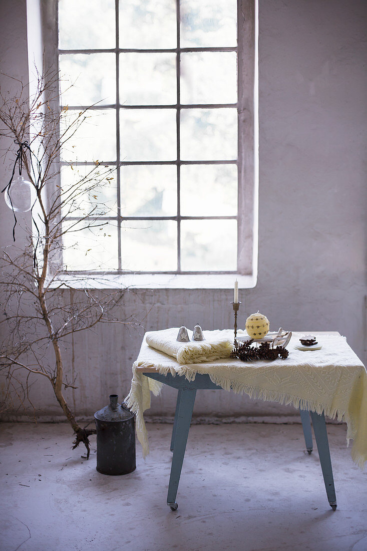 Woollen blankets and wintry accessories on table in front of industrial-style window