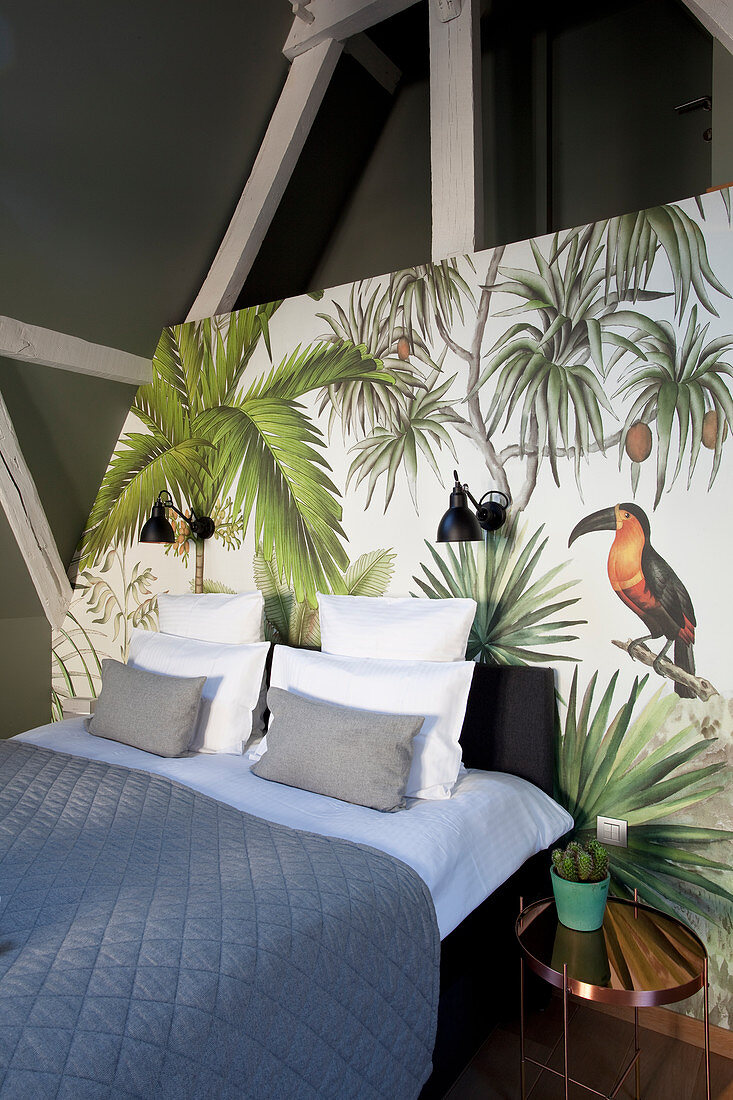 Doppelbett mit blauer Tagesdecke an Wand mit Dschungelmotiv