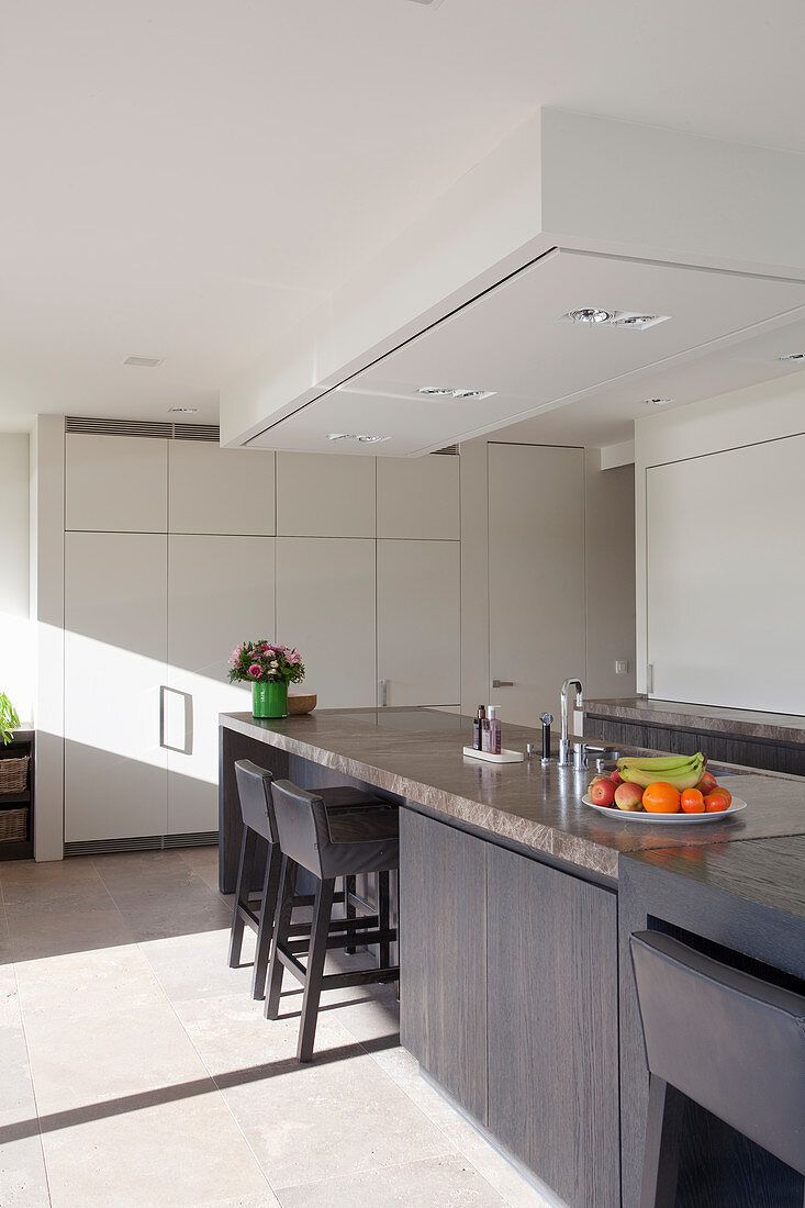 Island counter, barstools and white floor-to-ceiling fitted cupboards in elegant kitchen