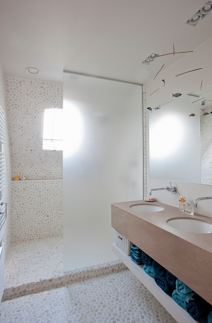 Waschtisch mit Doppelwaschbecken und Duschbereich mit Trennwand im Badezimmer mit Kieselsteinbelag