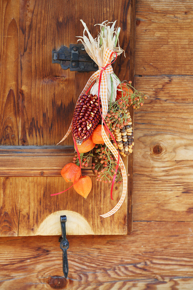 Hanging arrangement of multicoloured corncobs, physalis and rose hips