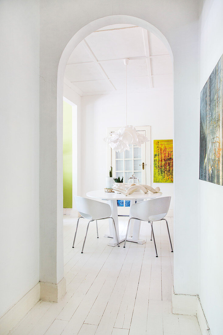 Blick durch Rundbogen-Ausschnittt auf weißen Tisch mit Stühlen