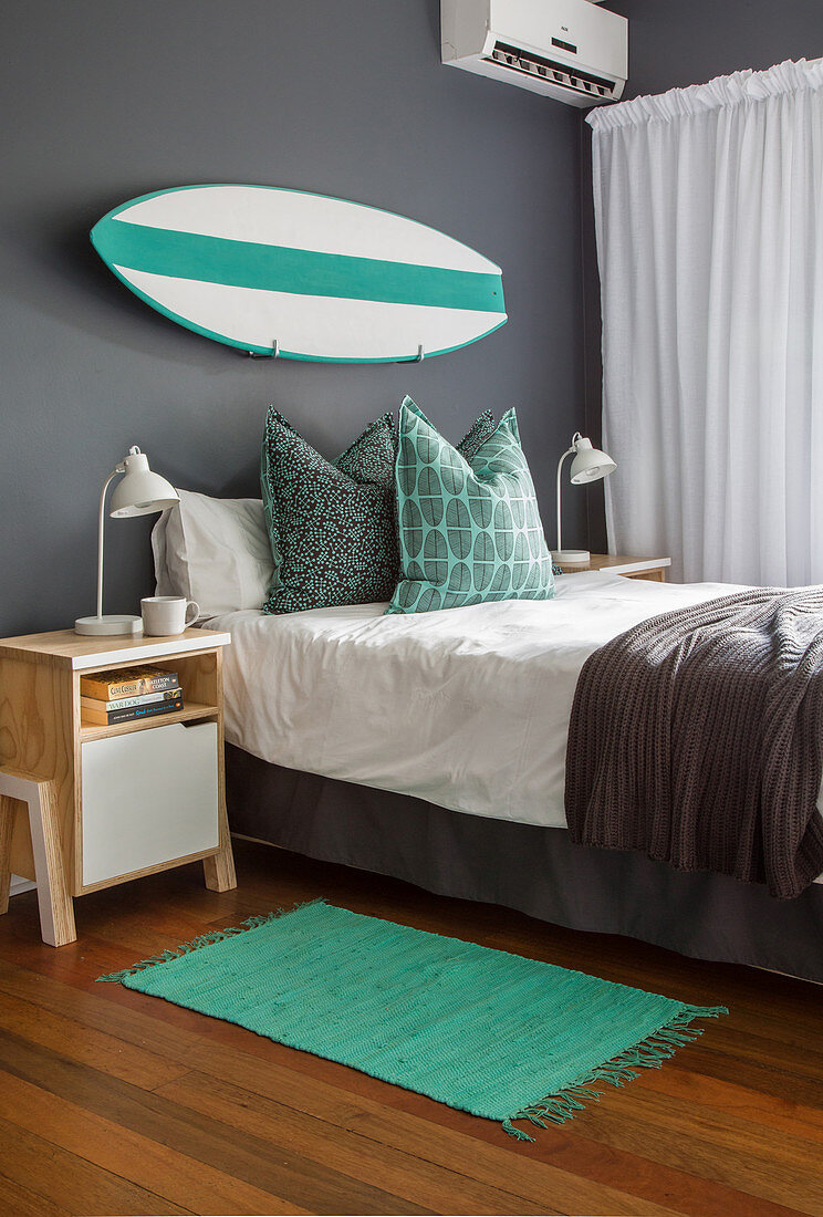 Bett vor grauer Wand mit Surfbrett