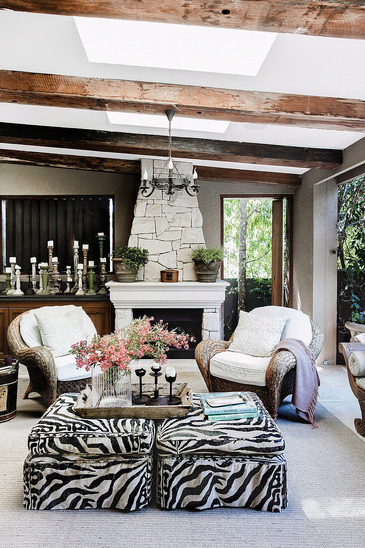 Rattan armchairs and ottoman with animal print in front of fireplace on living terrace