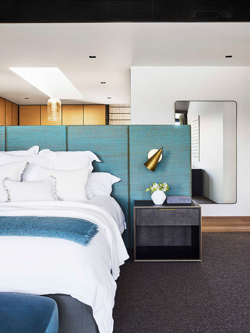 Doppelbett und Nachttisch an blauem Paneel als Bettkopfteil und Raumteiler im Schlafzimmer