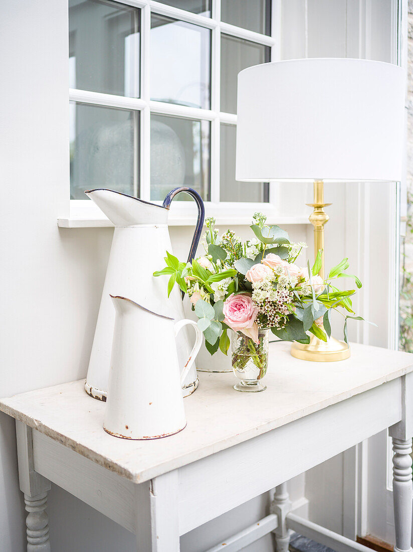 Old metal jugs, vase of flowers on lamp on small table