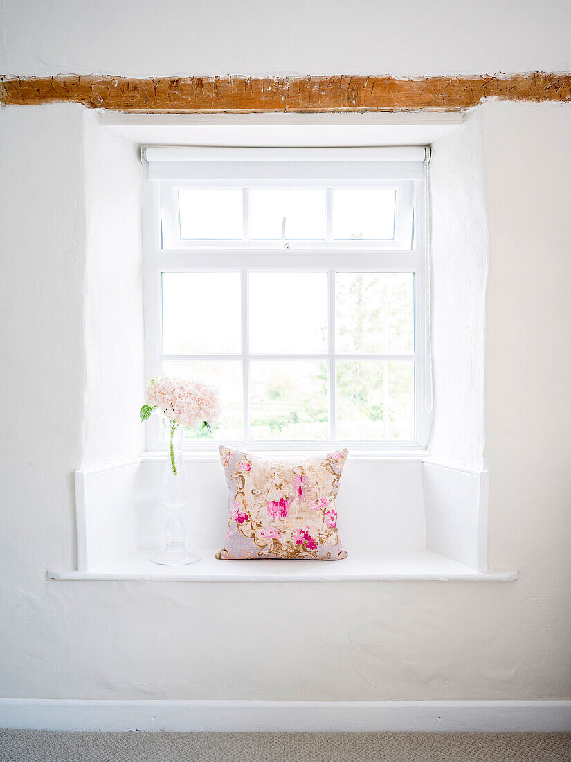 Sitzbank in der Fensternische mit geblümtem Kissen und Hortensie