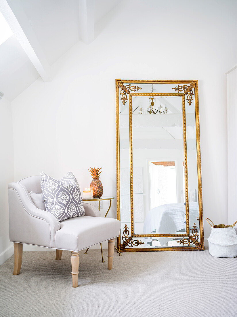 Armchair next to vintage-style full-length mirror with gilt frame