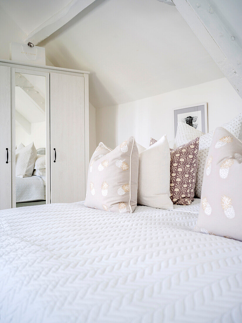 Scatter cushions arranged on bed in bedroom decorated entirely in white