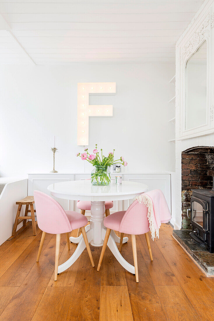 Large letter F on wall above pedestal table and pink retro chairs