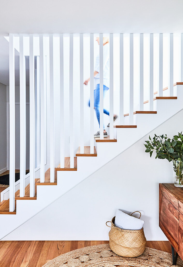 Treppe mit Geländer aus weißen Stelen, Sideboard mit Blätterzweig und Korbtasche auf dem Boden