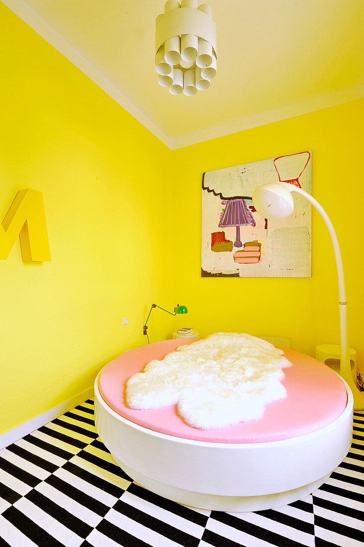 Round bed and standard lamp in bedroom with yellow walls and lack-and-white striped carpet