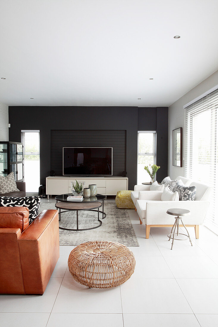 Fernseher vor schwarzer Wand, weiße Designersessel, Couchtisch und brauner Ledersessel in elegantem Wohnzimmer