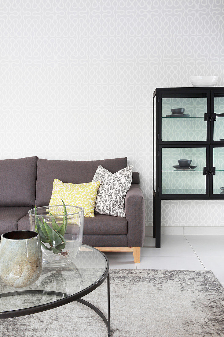 Graues Sofa, Couchtisch mit Glasplatte und Vitrinenschrank im Wohnzimmer