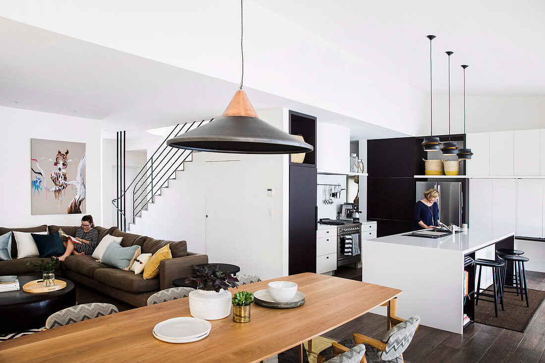 Schwarz-weiße Einbauküche, langer Esstisch und Lounge mit Polstersofa in offenem Wohnbereich